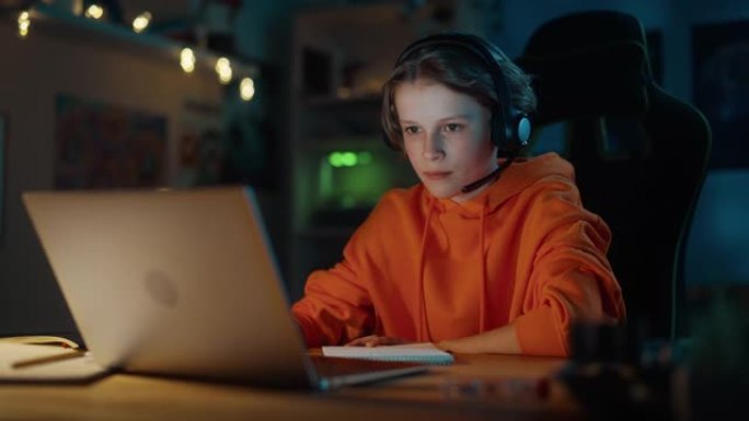 戴着耳机的聪明小男孩在家舒适的黑暗房间里，在笔记本电脑上参加在线课程。快乐少年在线浏览教育研究，笔记