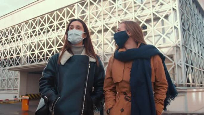 两个年轻快乐开朗美丽的女性朋友戴着医用口罩在现代阳光城大厦散步，聊天