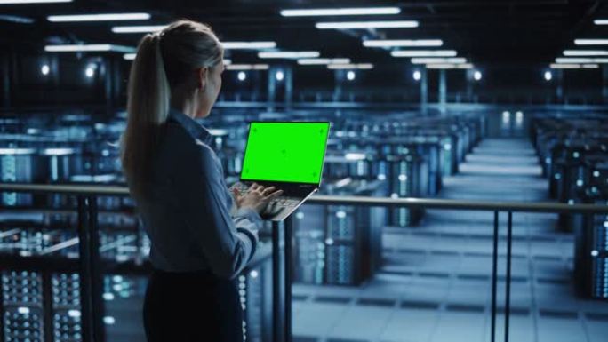 在数据中心使用色度键笔记本电脑的女性It专家。大服务器场云计算设施，维护工程师与绿屏计算机合作。肩部