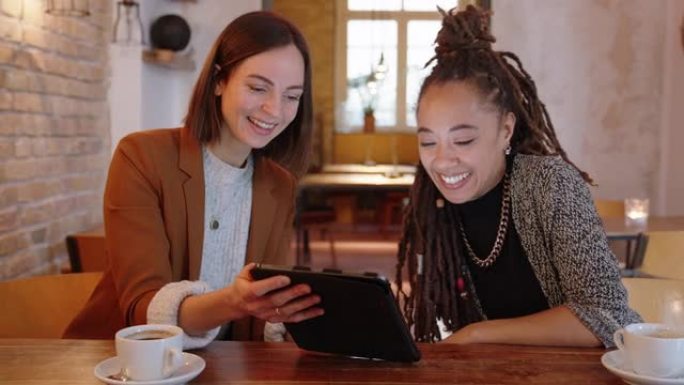 两名女商人坐在咖啡馆里，使用数字平板电脑