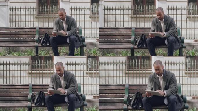 英俊的商人在公园长椅上浏览外面的平板电脑。严肃的男性滚动社交媒体应用程序，同时独自在公园放松。时尚的