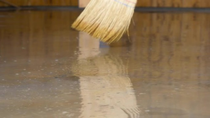 低角度: 面目全非的人用稻草扫帚扫过被水淹没的地板。