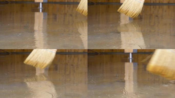 低角度: 面目全非的人用稻草扫帚扫过被水淹没的地板。