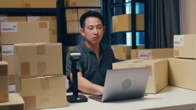 亚洲商人使用条码机扫描纸盒中的客户数据，并在笔记本电脑中输入注册在线信息订单详细信息，以便在仓库发送