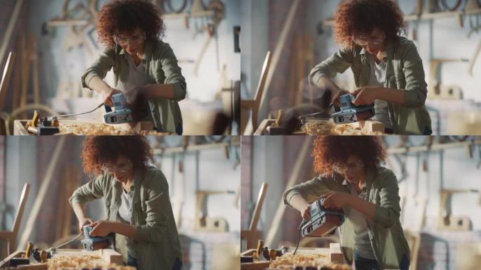女木匠戴着防护安全眼镜，使用电动皮带砂光机在木条上工作。艺术家或家具设计师在车间从事产品创意。