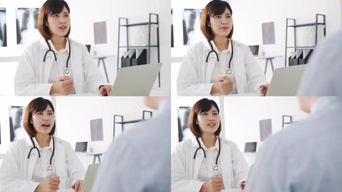 年轻的亚洲女医生使用电脑笔记本电脑正在发表重大新闻谈话，讨论结果或症状与男性患者坐在健康诊所的桌子上
