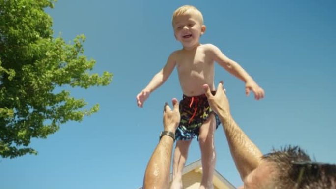 低角度视角的父亲在游泳池玩耍时将他的宝贝儿子抛向空中
