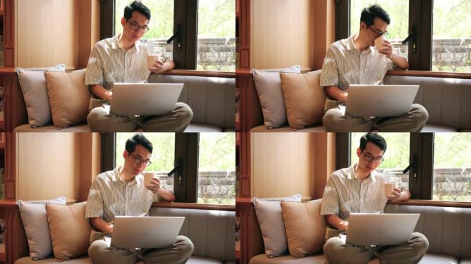 男人用笔记本电脑坐在靠窗的沙发上