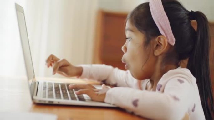 小女孩在家学习在笔记本电脑上打字。儿童在虚拟课堂期间在线工作和互动。学龄前儿童享受使用现代技术的惊人
