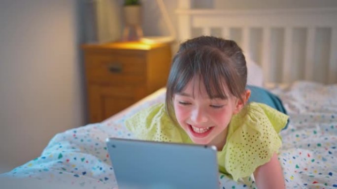 卧室里的女孩躺在床上播放音乐或在数字平板电脑上看电影-慢动作拍摄