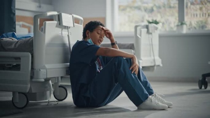 医院重症监护冠状病毒病房: 悲伤的肖像，疲倦的黑人护士脱下口罩坐在地板上，为所有因大流行而丧生的患者