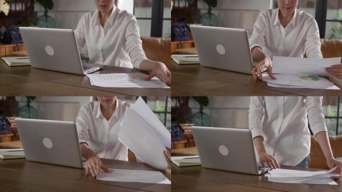 专注于一个女人用笔记本工作的手，并在房间的桌子上寻找文件。只握住她正在工作的手