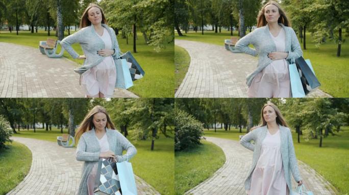 未来母亲在城市公园行走的慢动作背痛背着购物袋