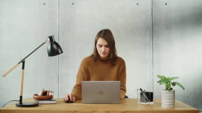 专业的创意女人坐在办公室的办公桌前，在笔记本电脑上工作。时尚的办公空间设计非常适合从事电子商务项目的