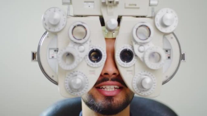 用验光机做眼睛测试的男性患者。一个年轻人在眼科中心或眼科诊所接受检查的特写镜头。那家伙一边说话，一边