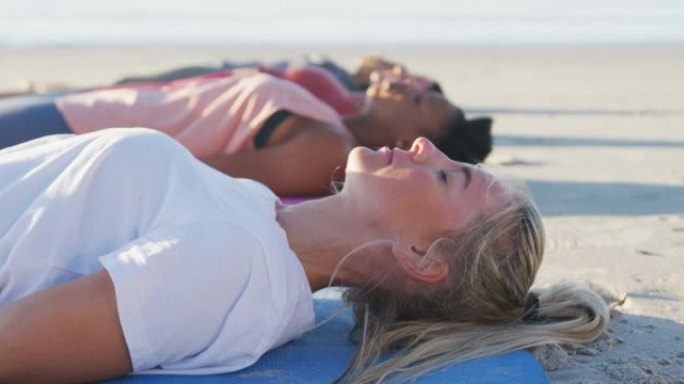 一群练习瑜伽的女性朋友，躺在沙滩上的垫子上