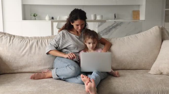 母亲和小女儿坐在笔记本电脑的沙发上