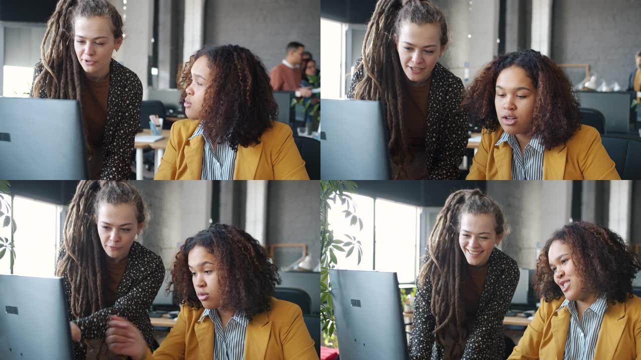 快乐的女孩高加索人和非洲裔美国人在工作场所使用计算机交谈