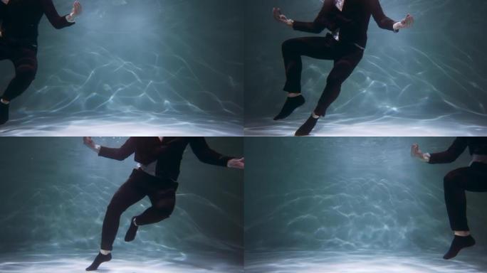 黑色公司套装有趣快乐的愚蠢商人在水下慢动作下做有趣的螃蟹舞蹈的电影镜头。