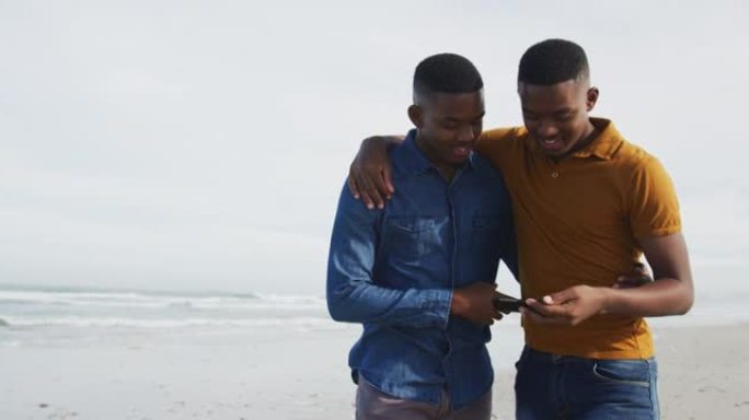 使用智能手机站在海滩上的非洲裔美国双胞胎兄弟