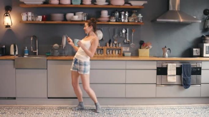 4k视频片段，一名年轻女子在家里喝咖啡和在厨房跳舞时使用电话