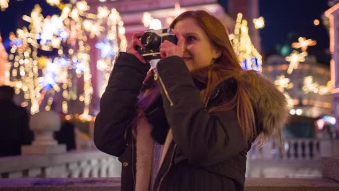 女人用老式相机拍摄圣诞节装饰城市