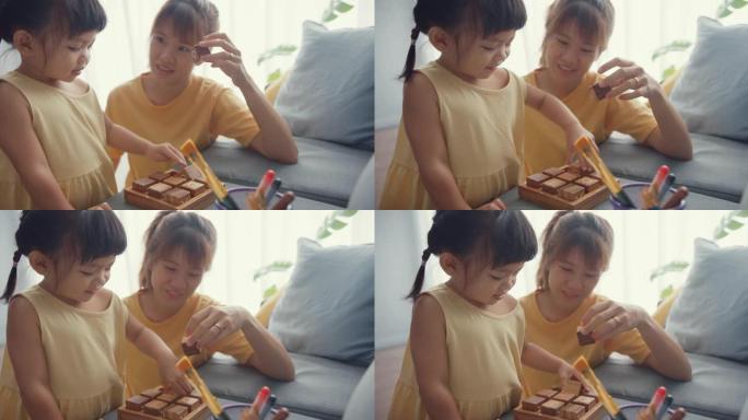 快乐快乐的亚洲家庭妈妈教女孩玩棋盘游戏爱好用木箱玩得开心在家里客厅的沙发上放松。