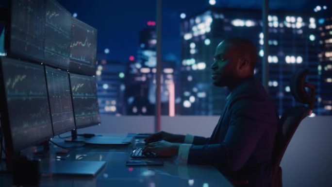金融分析师在计算机上工作，具有实时股票，商品和交易所市场图表的多显示器工作站。非裔美国商人深夜在投资
