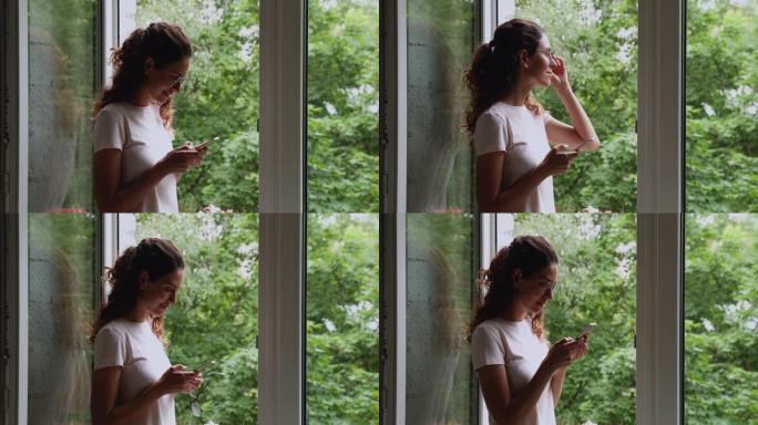 站在开着的窗户旁边拿着智能手机的女人感觉无忧无虑