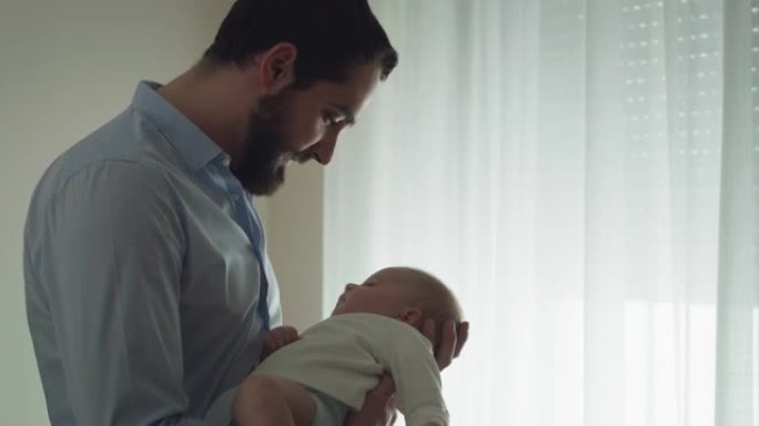 一个年轻的和平父亲的电影镜头正抱着他刚出生的男婴，同时在日光下睡在窗户上。甜梦，童年，生活，父亲身份