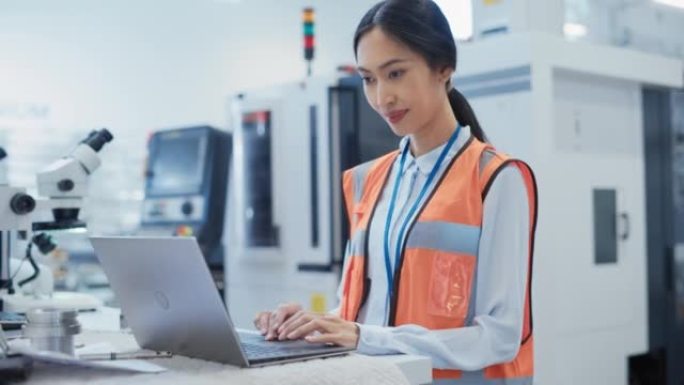 一位穿着橙色安全背心的亚洲女工程师在电子制造工厂的笔记本电脑上工作的肖像。处理日常任务和研发数据的技