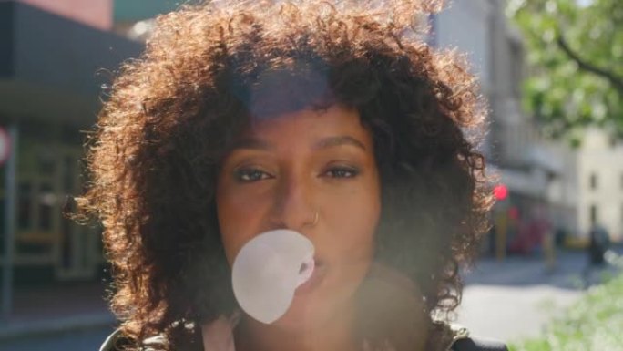 年轻时髦的女孩在户外吹泡泡糖。酷，年轻的美国黑人女性，脸上带着顽皮的表情，用口香糖制造了一个大泡泡。