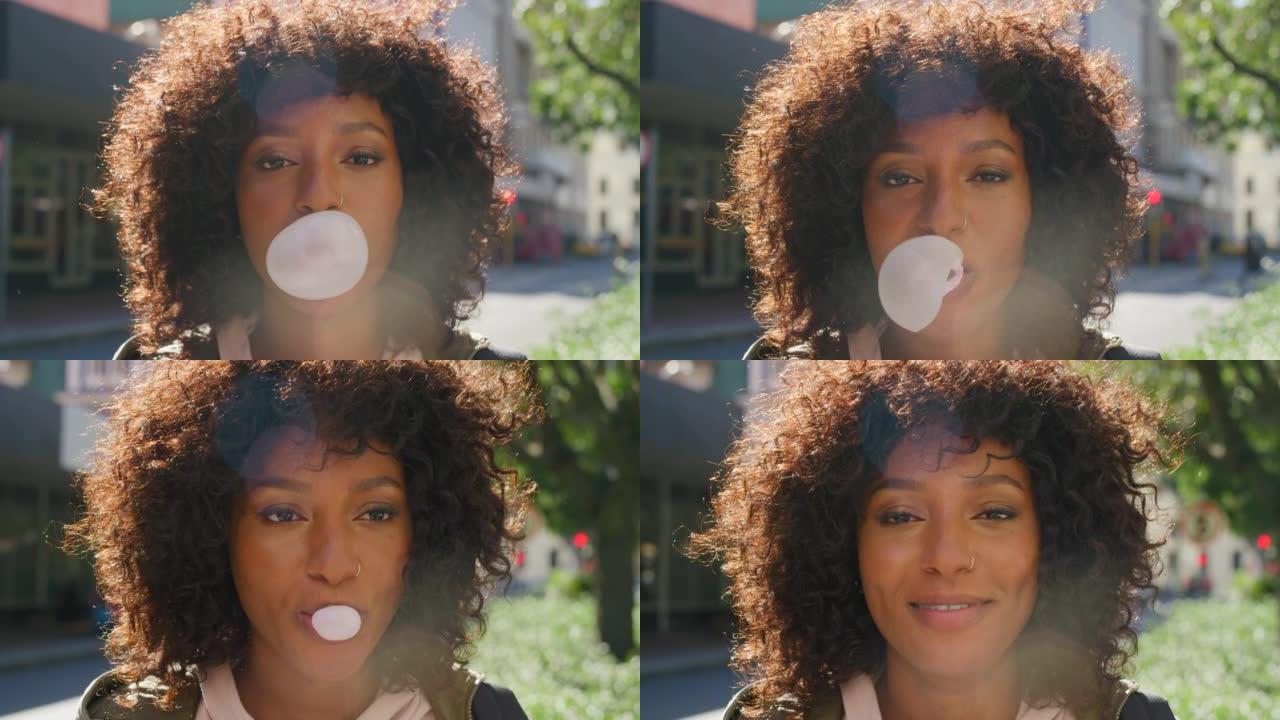 年轻时髦的女孩在户外吹泡泡糖。酷，年轻的美国黑人女性，脸上带着顽皮的表情，用口香糖制造了一个大泡泡。