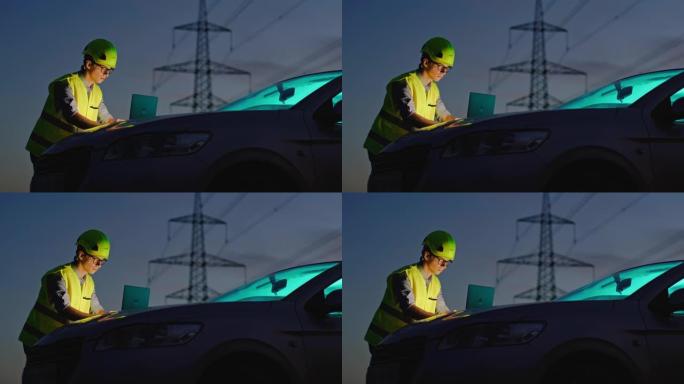 日落时，一名男性电气工程师在汽车引擎盖上的笔记本电脑上工作的慢动作镜头，背景为电源线