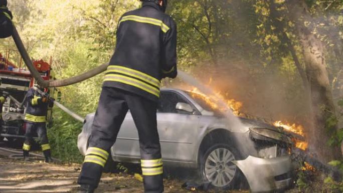 匿名消防员正在扑灭树旁汽车上的大火