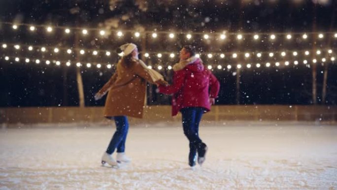 浪漫的冬天下雪的夜晚: 滑冰夫妇玩得开心，踏上溜冰场，开始跳舞。双人滑冰。年轻人拿着Halds。恋爱