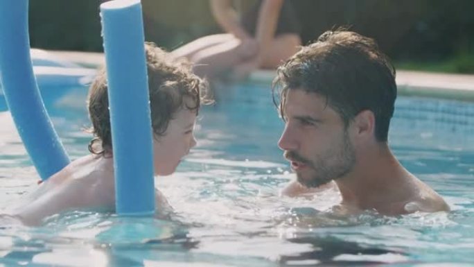父亲教儿子暑假在带浮标的室外游泳池游泳