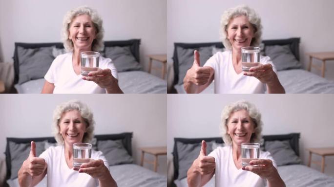 微笑的老妇人露出杯水和竖起大拇指。