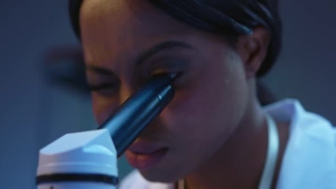 一位年轻的非洲裔美国科学家在显微镜下观察，我们在特写镜头中看到她