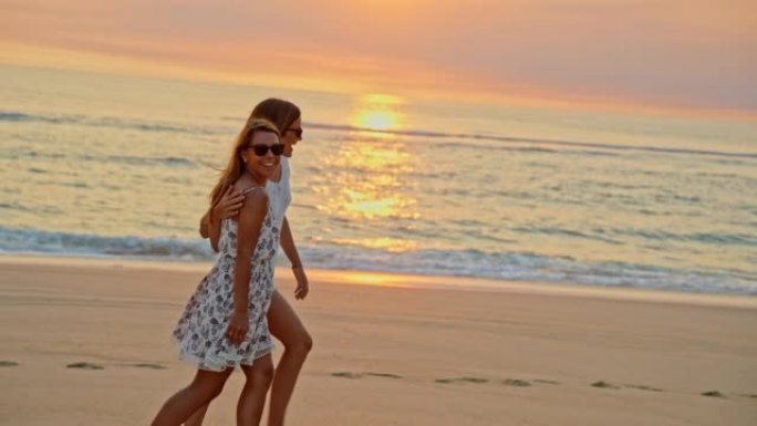 两个快乐的年轻女人在日落时在海滩上散步时拥抱