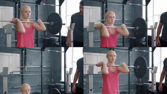 在健身房与教练一起进行杠铃深蹲训练的年轻女子的慢动作