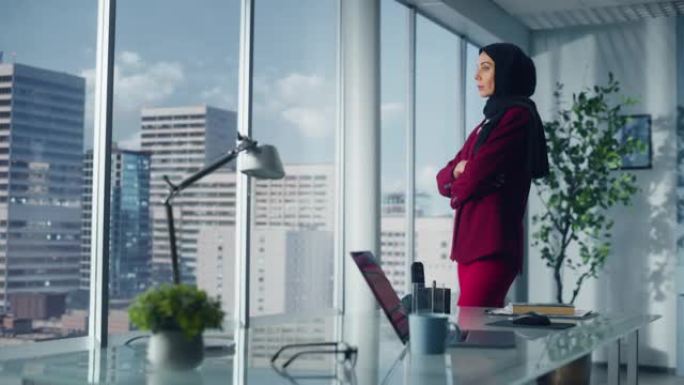 成功的穆斯林女商人穿着西装，站在办公室，站在大城市的窗外。自信的女性数字企业家为电子商务初创公司规划