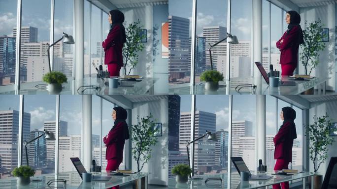 成功的穆斯林女商人穿着西装，站在办公室，站在大城市的窗外。自信的女性数字企业家为电子商务初创公司规划
