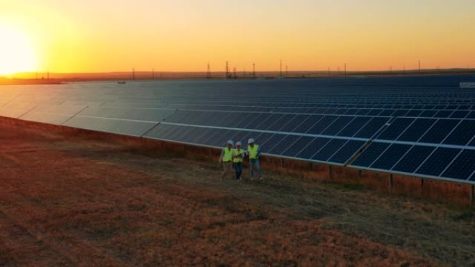 工程师们在日落时沿着太阳能领域行走。可再生能源，太阳能发电概念。