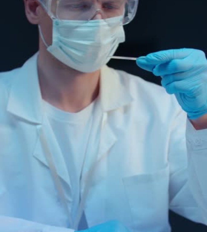 一位穿着实验室外套和防护面罩的严肃的白色化学家在现代实验室中与显微镜载玻片一起工作，我们在特写中看到