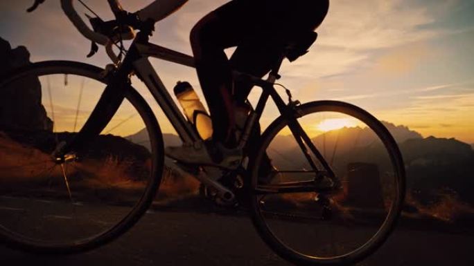 剪影的自行车手在日出山上的道路上坡骑行