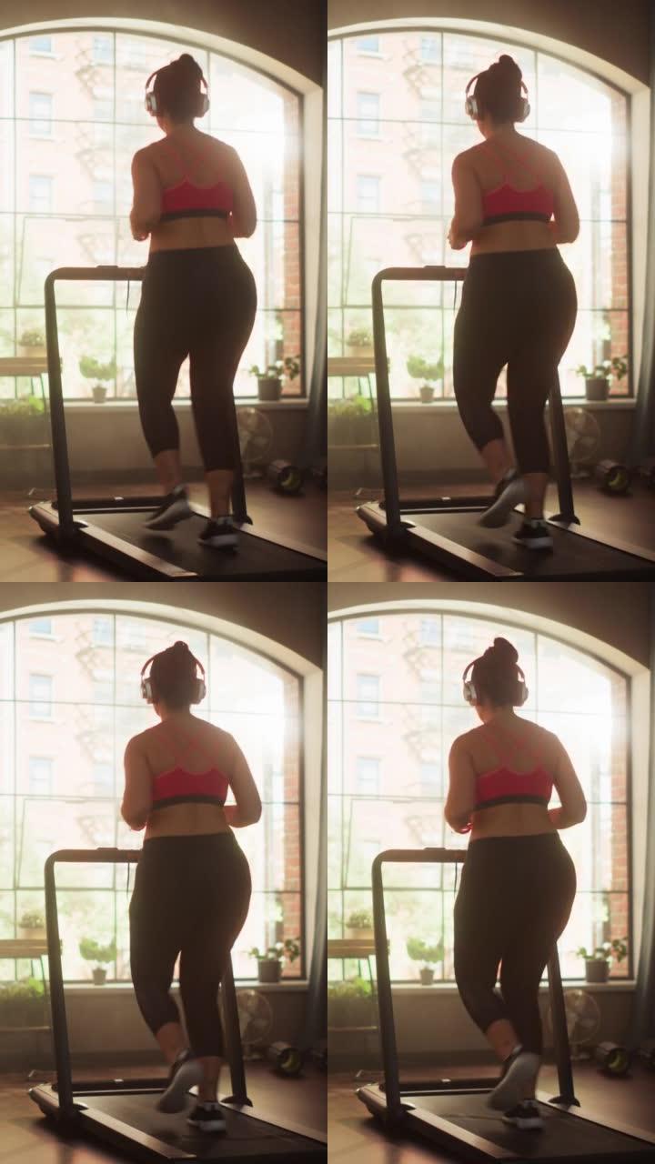 垂直屏幕。美丽的运动加体型积极的运动女人在家里的健身房跑步机上跑步。精力充沛的女运动员训练，一边听播