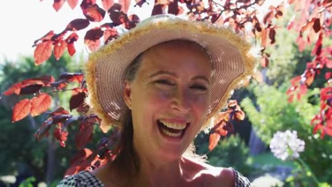 快乐的高加索高级妇女在花园里戴着遮阳帽，在阳光下微笑的肖像