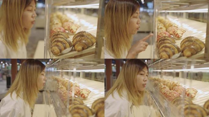 亚洲妇女在面包店架子上看着羊角面包的品种