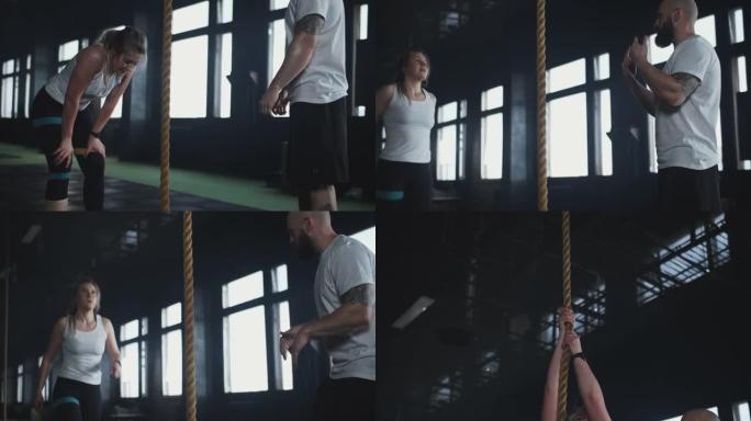 美丽的年轻运动金发女子在现代健身房锻炼中与专业男教练一起练习绳索攀爬